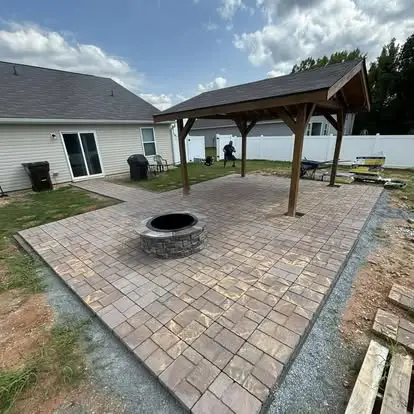 Paver patio with a round stone fire pit and a timber pergola behind a home, built by Miser Landscaping